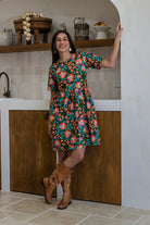 Woman wearing a 100% cotton relaxed fit dress with round neckline and short sleeves in olive green based floral print.