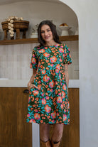 Woman standing with one hand in pocket of a 100% cotton dress in olive green based floral print