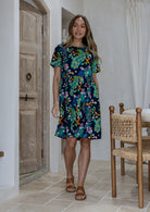 Woman wearing a above knee length floral cotton dress with short sleeves, pockets and round neckline 