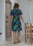 Woman standing backwards wearing a 100% cotton navy blue based floral relaxed fit dress with round neckline and short sleeves.