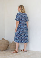 Woman stands backwards wearing a 100% cotton relaxed fit short sleeve dress in navy based floral print. 