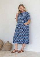 Model poses in relaxed fit cotton midi length dress with short sleeves and high round neckline with one hand in pocket