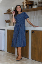 Woman wearing a 100% cotton relaxed fit dress in navy based white striped print with round neckline 