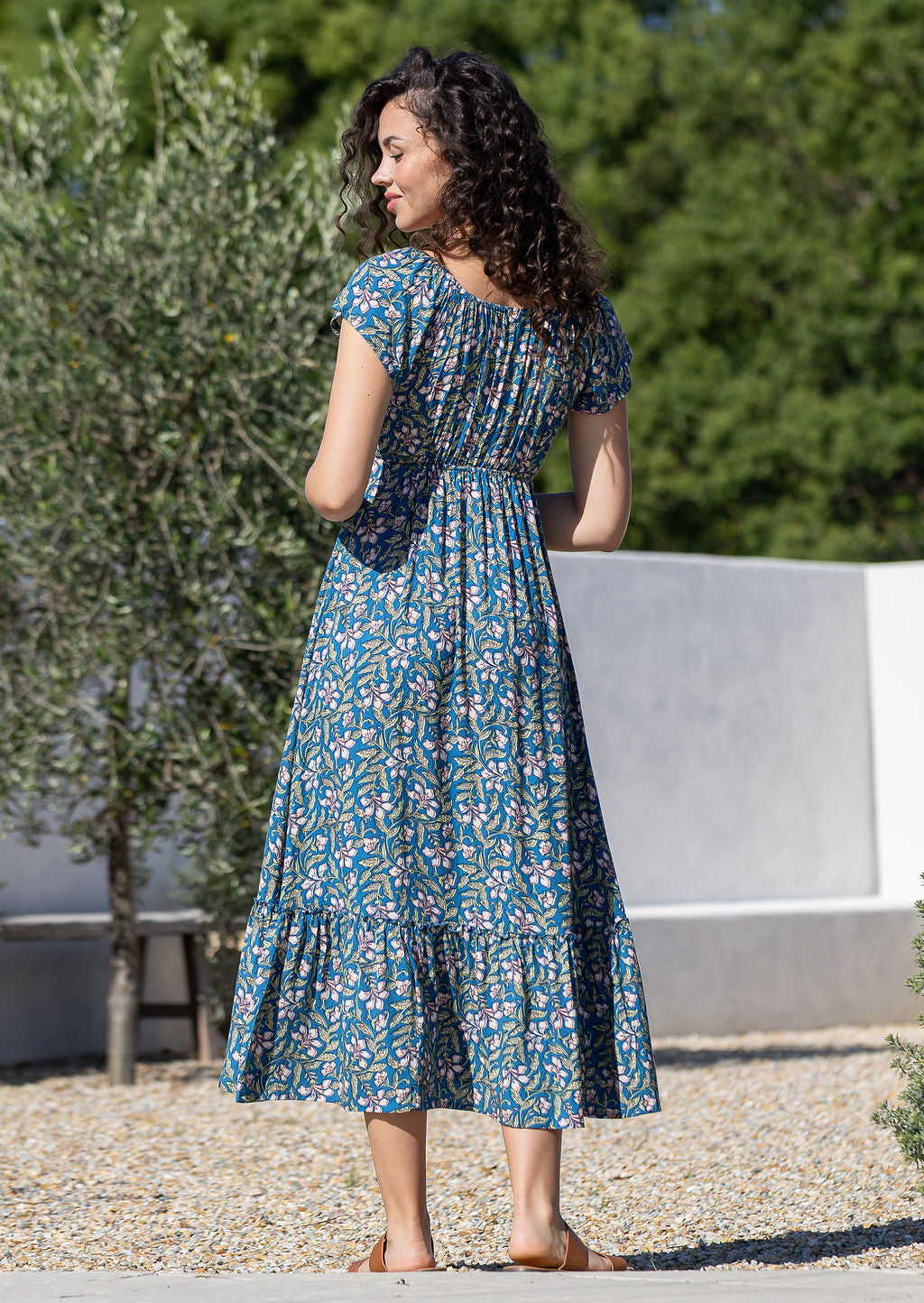Back view of model wearing 100 percent rayon maxi dress in blue based floral print