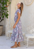 Model looking up over her shoulder wearing 100 percent rayon maxi dress in blue based floral print