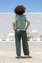 Woman stands backwards wearing a 100 percent cotton loose cut blouse in sage green based floral print and plain green pant. 