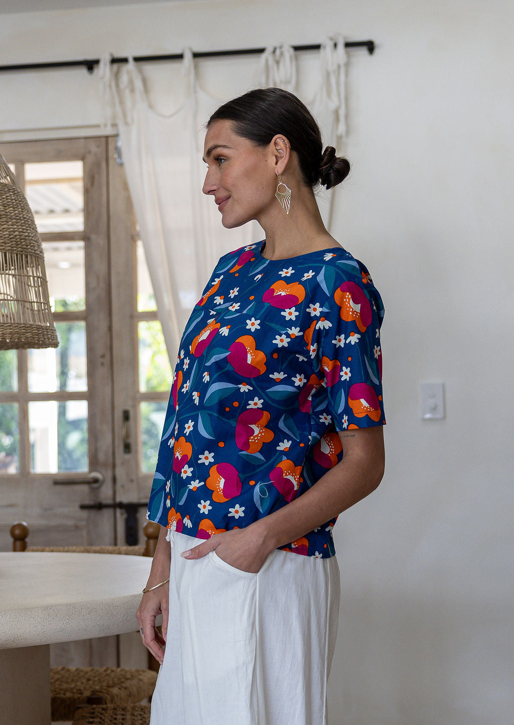 Woman standing sideways wearing a relaxed n fit royal blue based printed cotton top. 