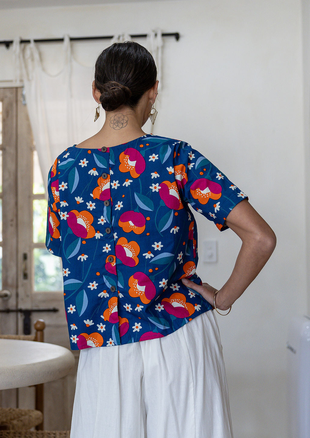 Woman standing backwards wearing a relaxed n fit royal blue based printed cotton top with decorative buttons down the centre back
