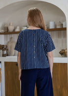 Back view of woman wearing relaxed fit navy and white striped cotton top with decorative buttons down the centre back