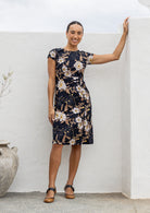 Woman wearing 100% cotton black based floral sundress with round neckline, cap sleeves, A line skirt and pockets
