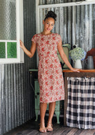 Woman wearing 100% cotton cream based floral sundress with round neckline, cap sleeves, A line skirt and pockets