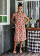 Woman wears a 100% cotton, knee-length A-line floral dress with both hands in pockets. 