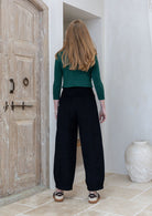 Woman stands backwards wearing a black cotton corduroy pants paired with green basic top