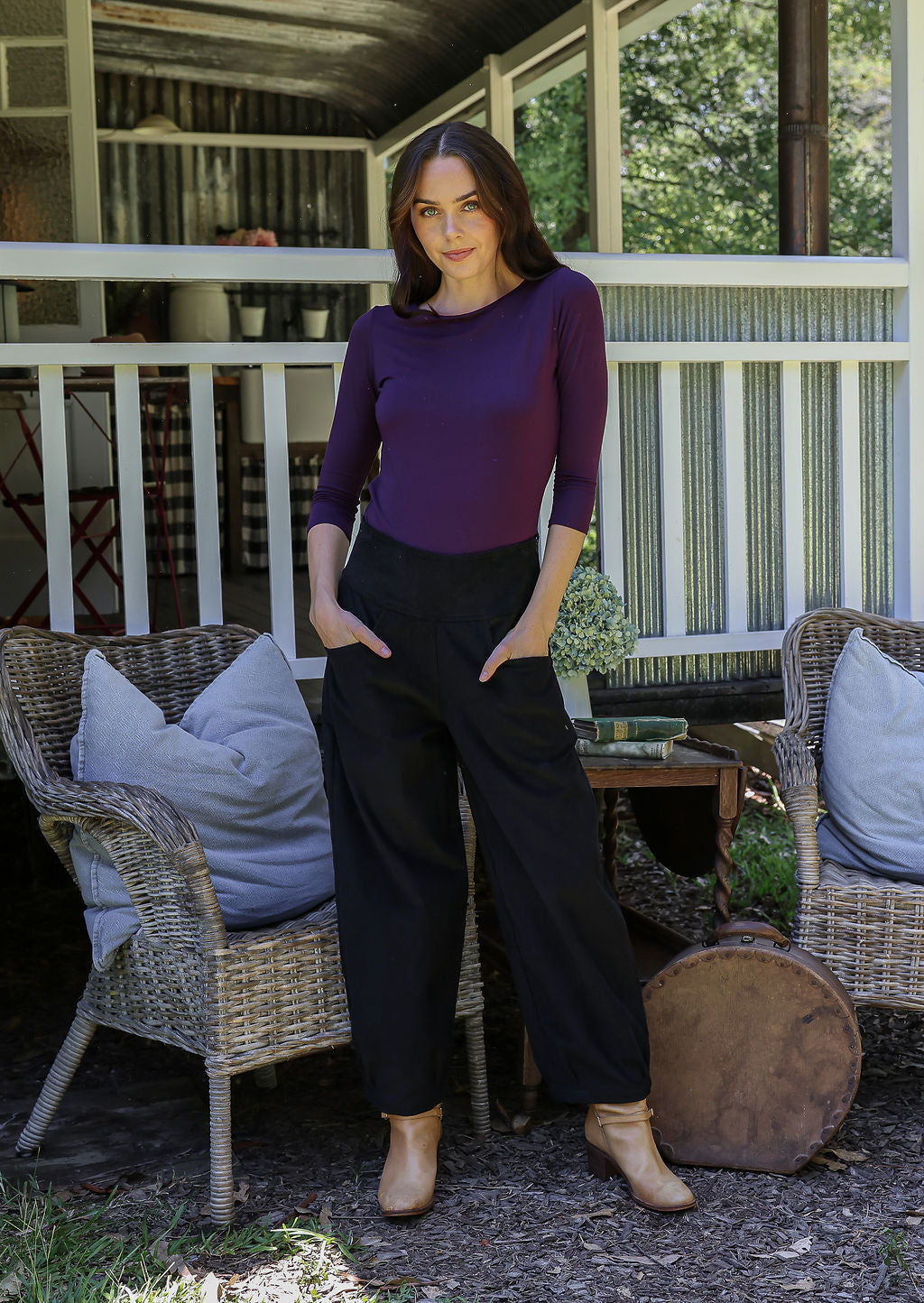 Woman standing in front of a porch wearing black cotton corduroy pants with hands in pockets