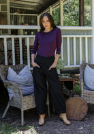 Woman standing in front of a porch wearing black cotton corduroy pants with hands in pockets