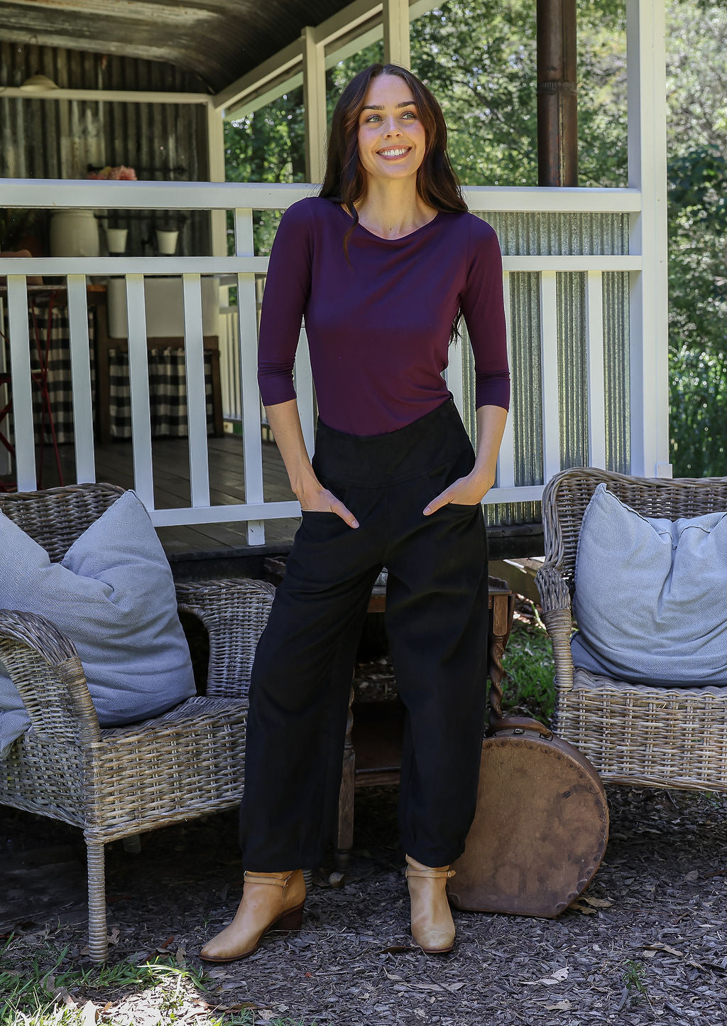 Woman posing in black cotton corduroy pants with hands in pockets, paired with a purple top and tan boots