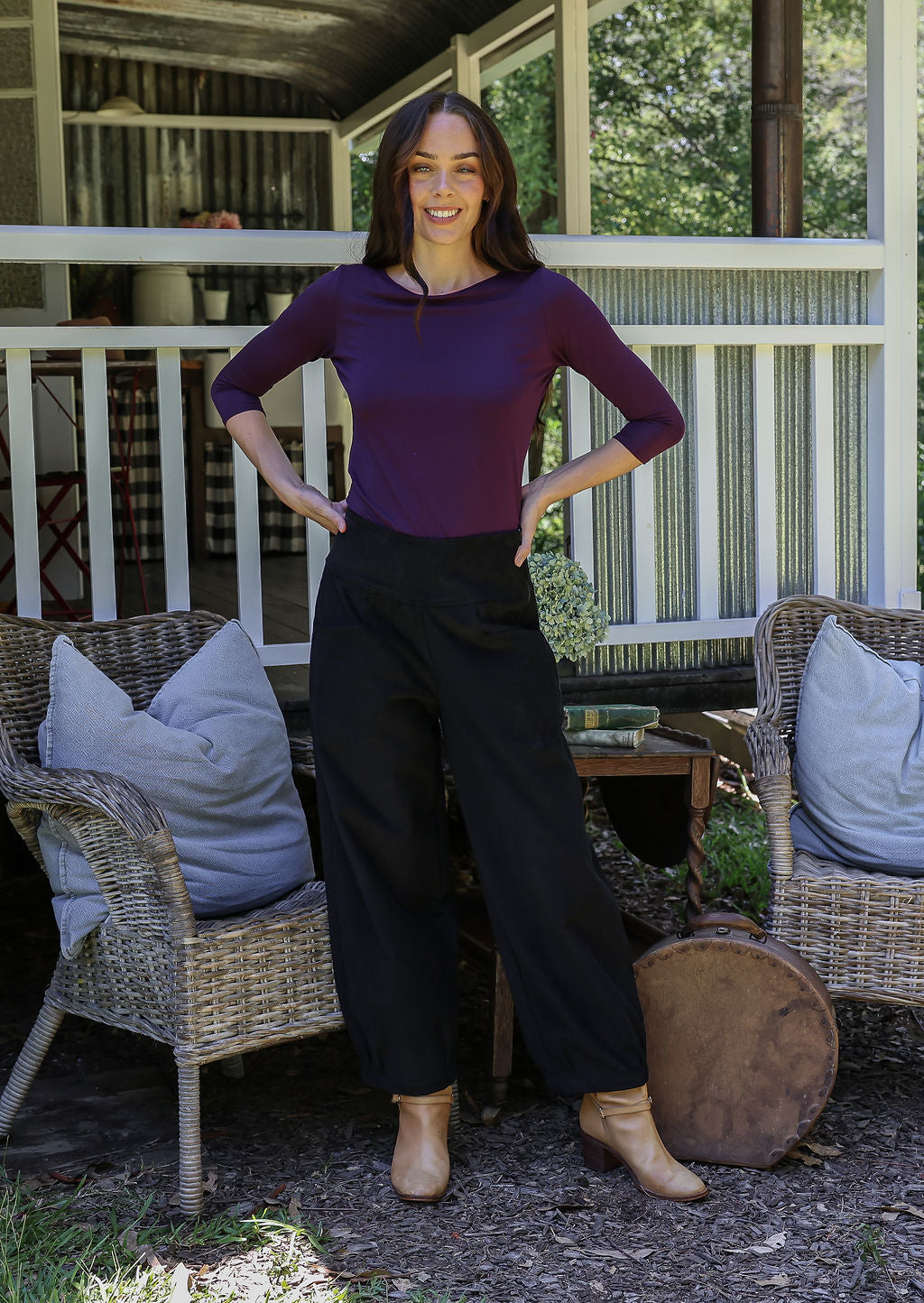 Woman standing with hands on hips wearing black cotton corduroy pants with wide leg and pockets, paired with purple top