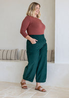 Model standing sideways wears corduroy wide leg pants with side zipper, pockets and small pleats at ankles.