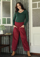 Woman posing in cotton corduroy wide-leg red pants with wide flat waistband, side zipper and small pleats at the ankles.
