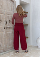 Woman stands backwards wearing a terracotta top and red pants