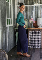 Model standing sideways wears corduroy wide leg pants with side zipper, pockets and small pleats at ankles.