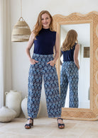 Woman posing in 100% cotton wide-leg navy based floral printed pants with wide flat waistband, side zipper and small pleats at the ankles.