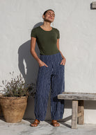 Woman posing in 100% cotton wide-leg navy based white strioed printed pants with wide flat waistband, side zipper and small pleats at the ankles.
