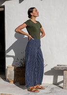 Model standing sideways wears 100% cotton wide leg pants with side zipper, pockets and small pleats at ankles.