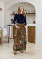 Woman wearing a green based multi-colour floral velvet wide leg pants with hands in pockets and a side zip
