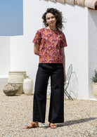 Woman wearing a 100% cotton loose fitting black top with short sleeves, round neckline and button back closure