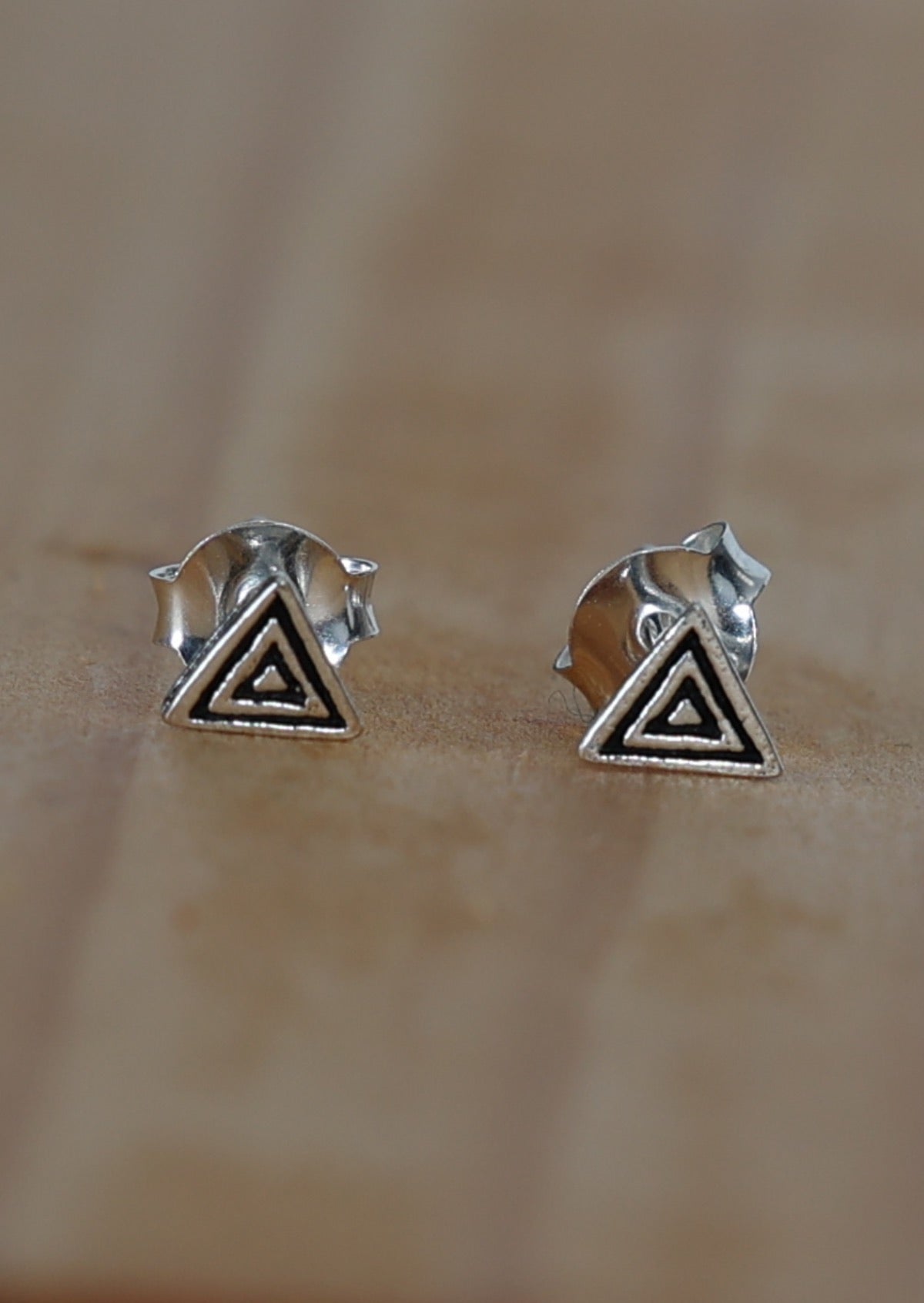 A pair of sterling silver triangular studs  with a rippled texture design, displayed against a wooden background 