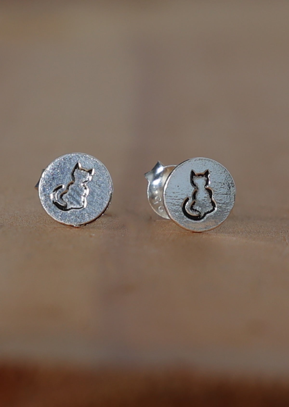 A pair of sterling silver stud earrings with a cat silhouette design pressed into the front