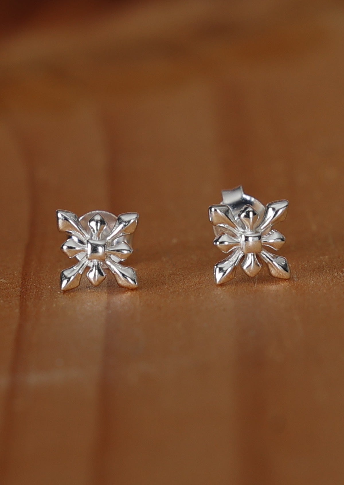 A pair of Deco Starflower silver stud earrings with a floral design, displayed against a wooden background