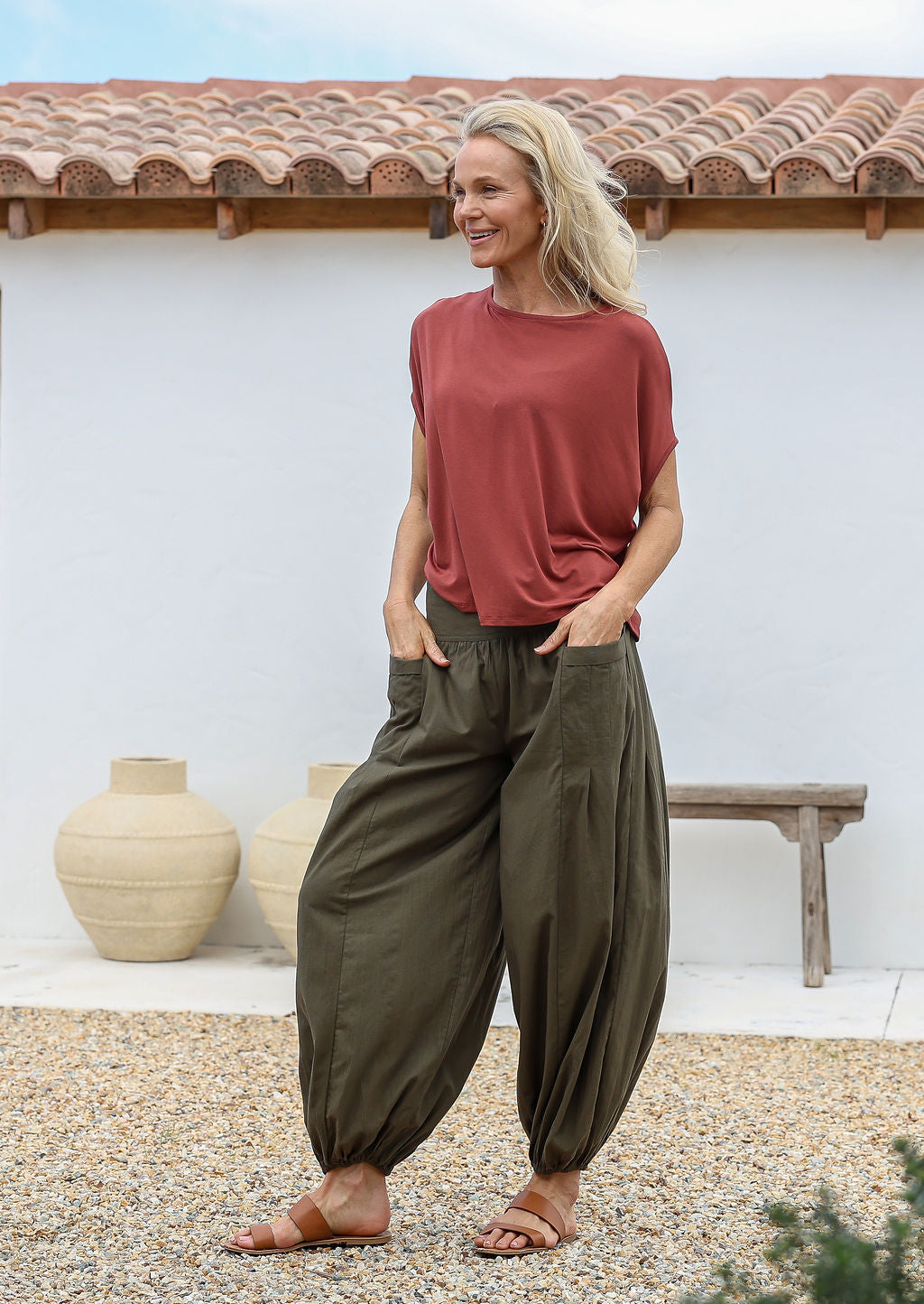 Woman with both the hands in pocket wears 100% cotton harem style pants in olive green with elasticated waist and ankles 