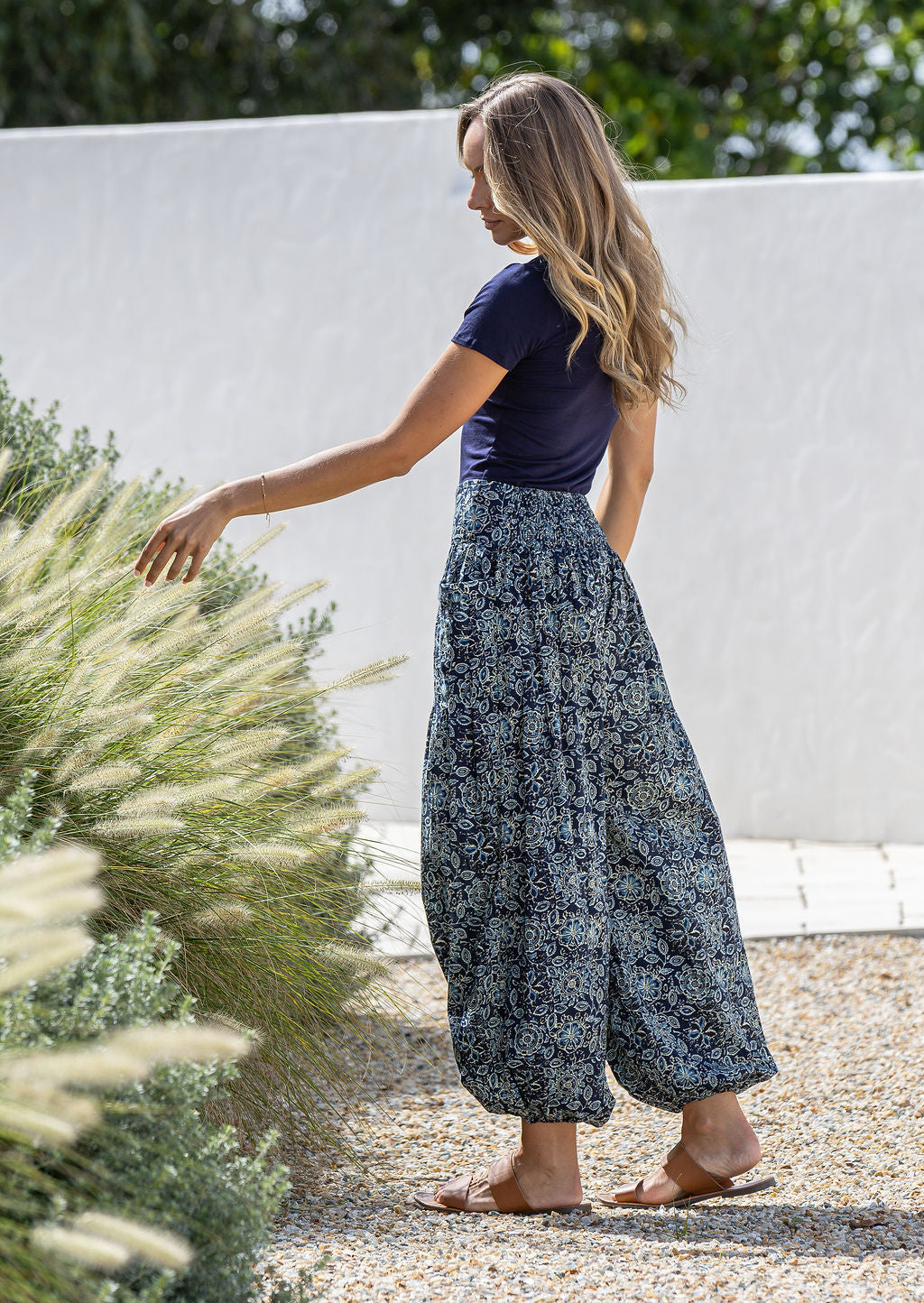 Woman holding flowers wearing a 100% cotton floral blue harem pants with flat wide waistband in front and elastic at the back.