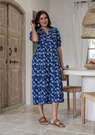 Woman wearing a 100% cotton dress in navy based floral print paired with tan sandals. 
