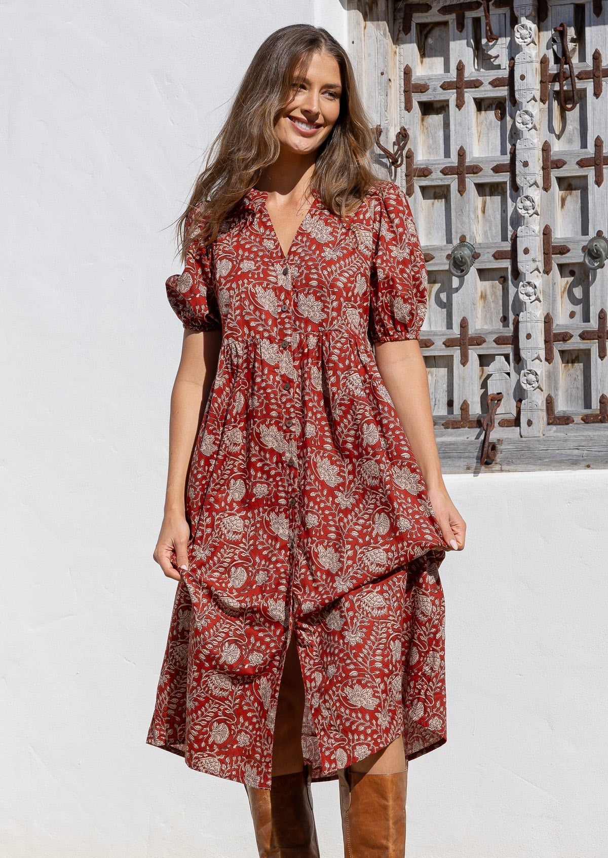 Woman wearing an earth red floral relaxed fit button through dress standing in front of a textured wall.