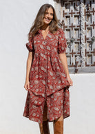 Woman wearing an earth red floral relaxed fit button through dress standing in front of a textured wall.