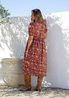 Woman standing backwards in a red floral cotton button through dress with elbow length puffy sleeves and a V-neckline.  