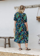 Woman standing backwards on in a navy floral cotton midi length dress standing outdoors