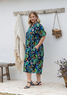Woman standing side on in a navy floral cotton midi length dress standing outdoors