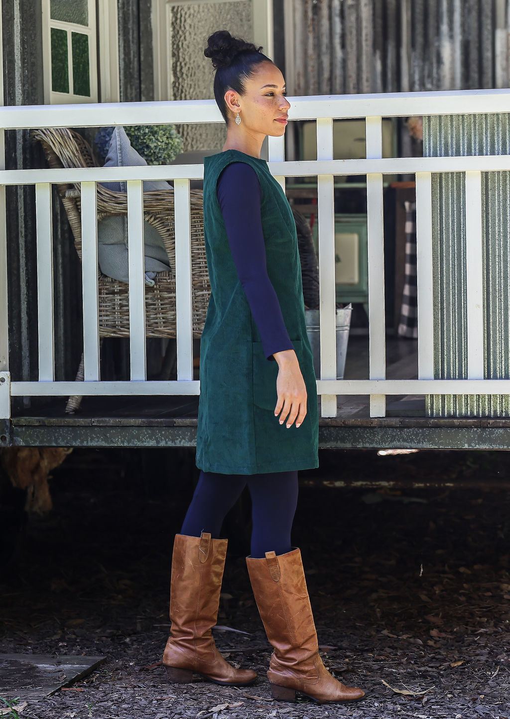 Woman wearing a green dress and brown boots standing in front of a white fence.