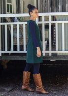 Woman wearing a green dress and brown boots standing in front of a white fence.