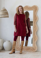 Woman poses in cotton corduroy tunic in cabernet paired with tan boots and leggings