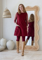 Woman poses in cotton corduroy tunic in cabernet with one hand in pockets styled with leggings and tan boots