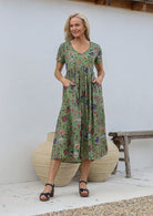 Woman standing with both the hands in pockets wearing a relaxed fit midi length cotton dress with empire waistline and gathered design.