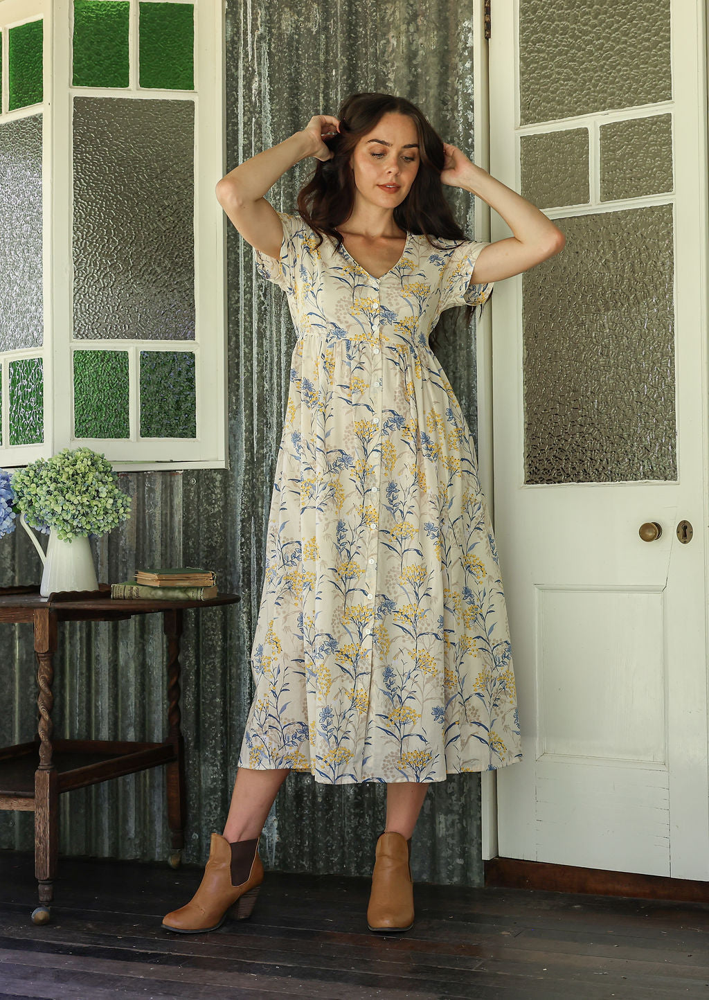 Woman in a white floral cotton dress standing on a verandah of a rustic cottage