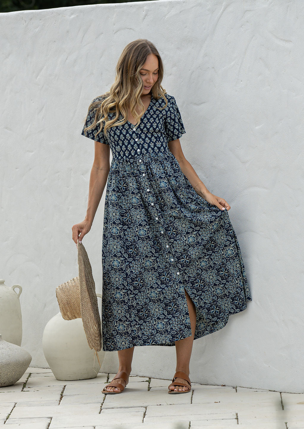 Woman standing in a 100% cotton floral print dress with a V-neckline, short sleeves, pockets, and buttons through to the knee.