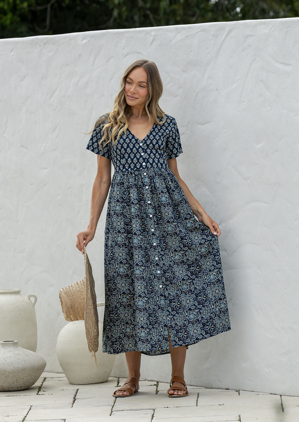 Woman wearing a relaxed fit, button through cotton dress in navy blue base floral print with V neckline.