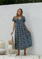 Woman wearing a relaxed fit, button through cotton dress in navy blue base floral print with V neckline.
